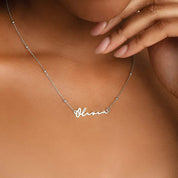 Collier prénom argent sur peau mate, la chaîne repose sur la clavicule