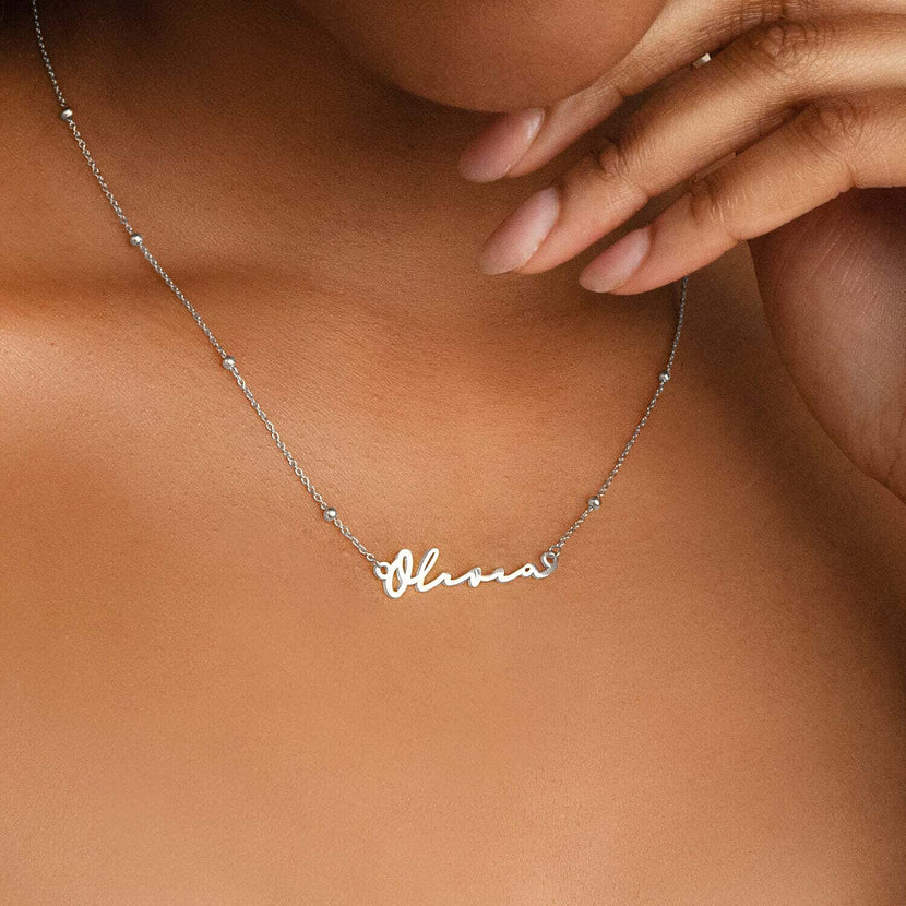 Collier prénom argent sur peau mate, la chaîne repose sur la clavicule