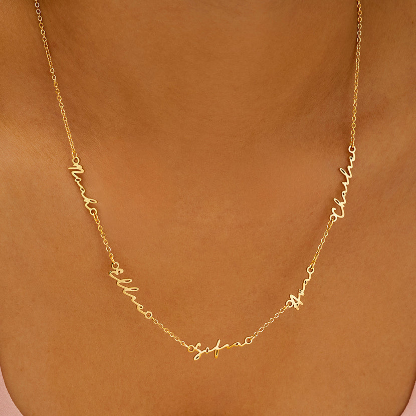 Collier 5 prénoms doré porté sur peau mate, les prénoms se suivent le long de la chaîne