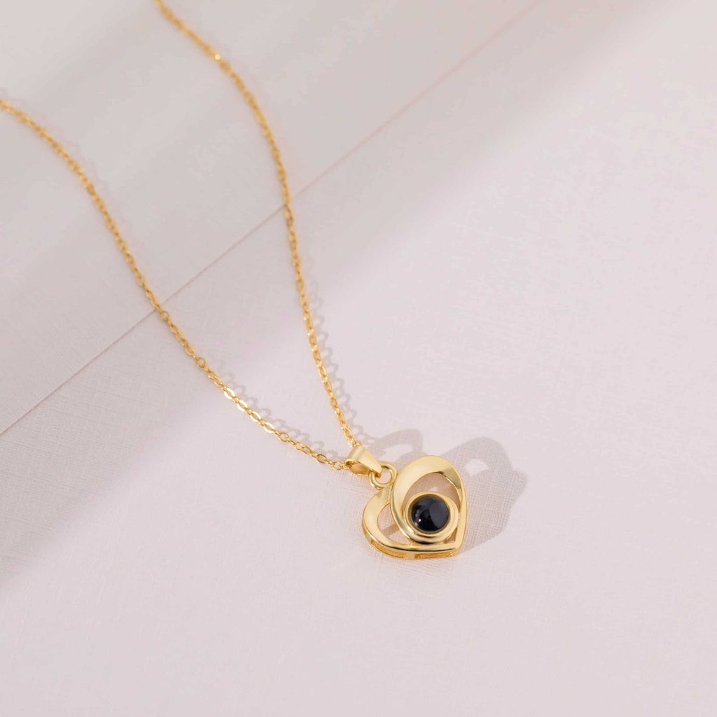 Pendentif cœur doré à projection photo posé sur fond rosé, collier personnalisé
