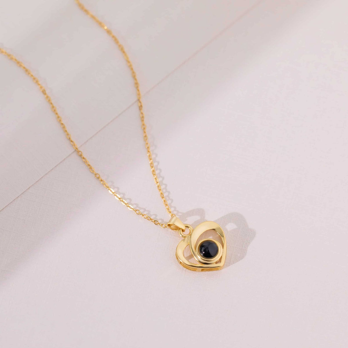 Pendentif cœur doré à projection photo posé sur fond rosé, collier personnalisé